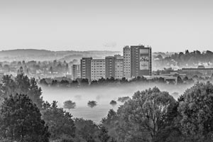 Großer Wohnkomplex inmitten einer nebeligen Landschaft mit vielen Bäumen und kleinen Häusern.